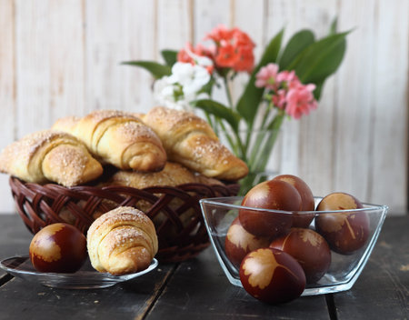 Easter background. Colored eggs and homemade rolls bagels in a natural plate on a dark wooden...