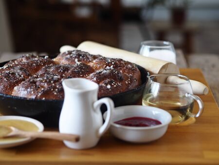 Homemade cake. Jam filled buns sprinkled with sesame and icing sugar in a baking pan on a kitchen cutting Board with ingredients and a Cup of tea.の写真素材