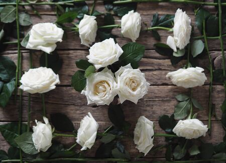 The concept of a floral frame.The view from the top.White roses with green leaves are arranged around the edges of a natural wooden table with three roses in the middle.A holiday greeting or message.の写真素材