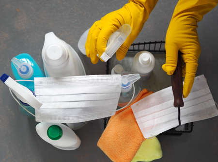 View from above. Plastic bottles with detergents and disinfectants on a gray background for cleaning and disinfecting at home. The woman's hands in a rubber glove take a basket of detergents.の写真素材