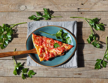 Natural homemade simple pizza with tomatoes, cheese, sausage and herbs. Cut piece of pizza on a wooden background.の写真素材