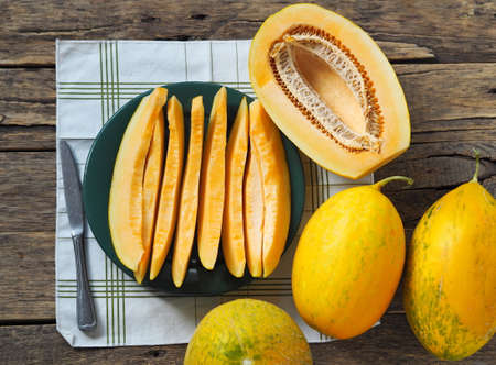 Food background. Melon slices with whole melons on a napkin on a wooden natural background.の写真素材