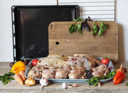 Raw wild duck carcasses in a tray with ingredients for cooking, against the background of a kitchen cutting board and an oven. Hunting season for birds. Preparing game.の写真素材