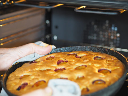 An elderly woman's hands take out a pan of ready-made apple and plum pie from the kitchen oven....