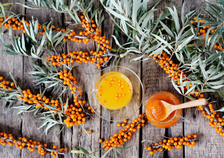 Tea with sea buckthorn jam with branches of fresh sea buckthorn berries on a wooden background. Copy...