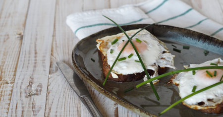 Two open sandwiches with dark rye bread with cheese, fried egg and green onions on a wooden white...