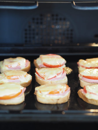Hot homemade sandwiches with sausage, tomatoes and cheese on a baking sheet in the kitchen oven....