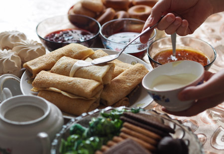 Food background with pancakes. Fragment of a table with food. Female hands lay the table, smearing stuffed pancakes with natural cream.の写真素材