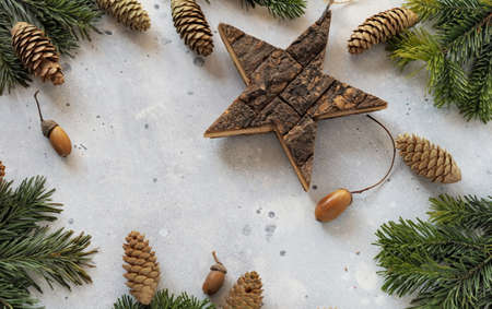 Concept for a congratulatory christmas background with Christmas tree branches, pine cones and a wooden decorative star on a gray wooden table. Copy space.の写真素材