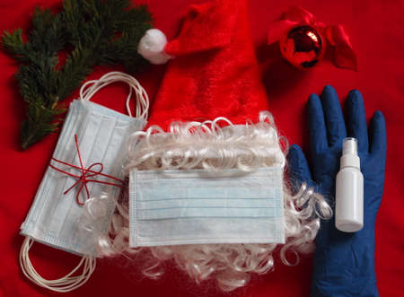 Santa Claus hat with medical mask, gloves and hand sanitizer on gray background. Use protective equipment to avoid getting Covid-19 during the Christmas periodの写真素材