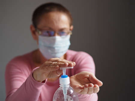 An elderly woman in a protective medical mask disinfects her hands to protect herself from the virus. Use personal virus protection. Blurred background.の写真素材