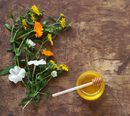 Honey and a spoon with honey on a wooden background with flowers. The concept of flower honey, organic natural healthy products.の写真素材