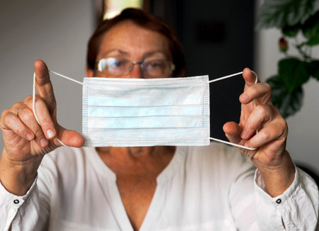An older woman holds a protective medical mask in the foreground