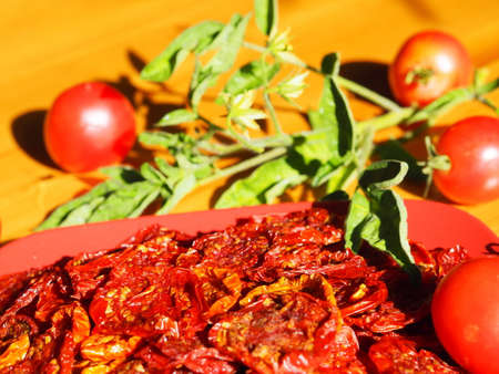 Sun-dried tomatoes in a red plate on a wooden table with a sprig of tops with yellow flowers. Evening sun. Horizontal format. Close-up.の写真素材