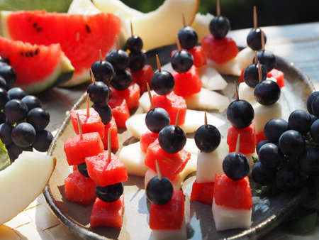Food background from fresh fruits. Canapes of grapes, pieces of watermelon and melon on a natural green background. Healthy eating.の写真素材