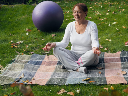 An elderly woman practices yoga in the fresh air. Yoga practice revives us to life, restores moral...