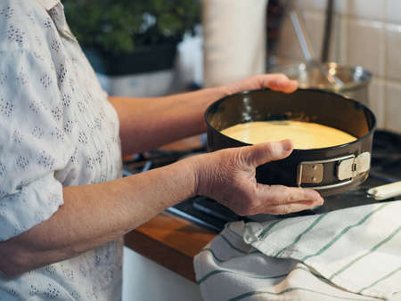The process of making a cake. Elderly woman's hands holding a baking dish with dough. Healthy homemade food.の写真素材