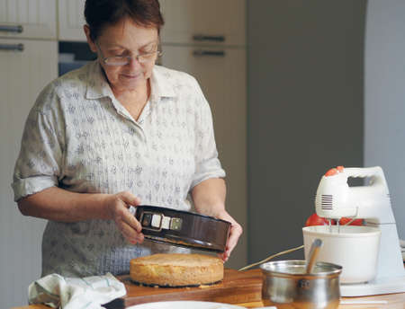 The older woman is busy with what she loves, making homemade cake. Preparing for a home holiday. Homemade healthy food. Hobby.の写真素材