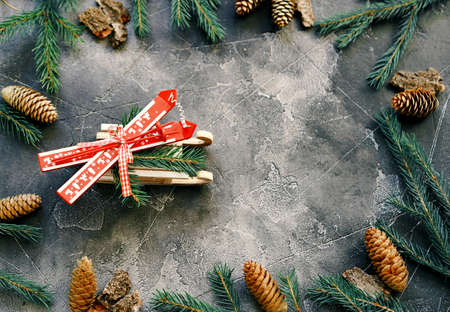Christmas greeting background with New Year is toys skiing on a sled surrounded by fir branches on a dark wooden background. Place for text.の写真素材