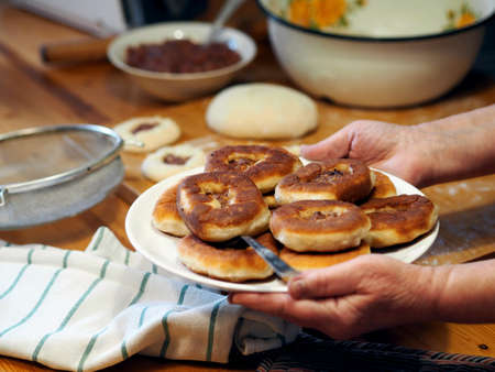 The process of home cooking whites, small pies with natural meat and the addition of vegetables. Elderly woman's hands hold a plate with whites on the background of the kitchen table. Healthy homemade food.の写真素材