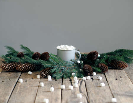 The process of decorating a house for Christmas. Fir branch, mini marshmallows in a mug with cocoa, burning candle on a wooden rustic background.の写真素材