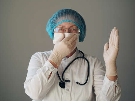 Kind elderly doctor in protective medical mask showing heart sign with hands in sterile gloves. The concept of a profession that saves lives and promotes charity.の写真素材