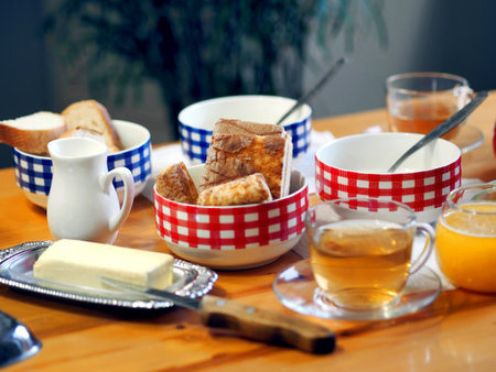 Everyday diet breakfast with butter, milk noodles in checkered tureens and tea with honey on the kitchen table. Side view.の写真素材