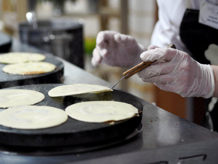 The guy cook in gloves pours a portion of batter with a ladle on an electric stove for baking...