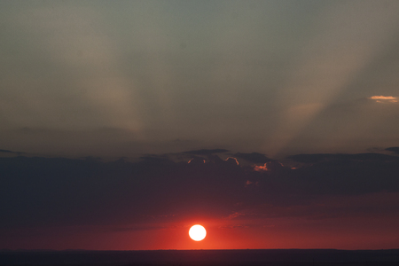 Natural sun exposure on field or meadow. Bright dramatic sky and dark earth. Countryside landscape under scenic colorful sky at sunset. Sun over the horizon. Warm colorsの写真素材
