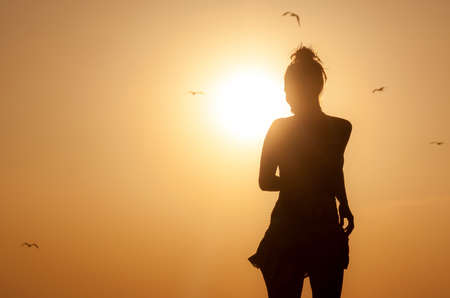 Silhouette young woman enjoying on the beach with a sunny sunset. Carefree person enjoying on vacationの写真素材