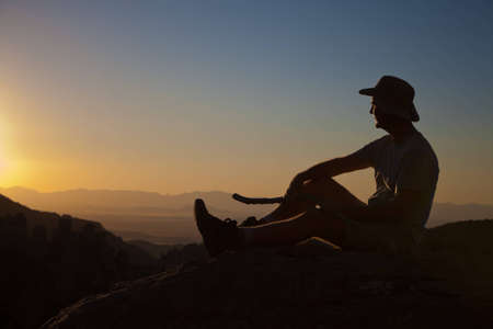 Mature man rest from hikingto enjoy the sunset on top of a mountainの写真素材