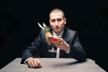 Elegant young man drinking cocktail on black background の写真素材
