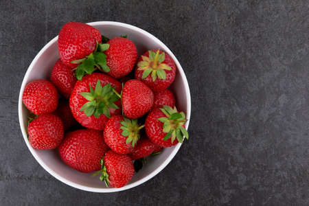 Strawberries in a saucer on a black stone backgroundの写真素材