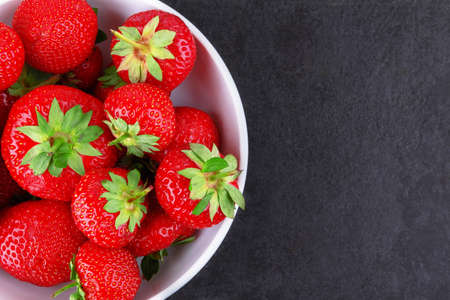 Strawberries in a saucer on a black stone backgroundの写真素材