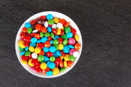 Colorful chocolate buttons on bkack stone surfaceの写真素材