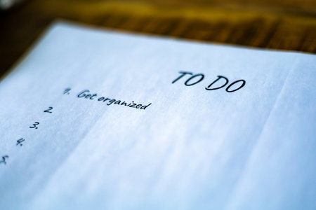 A white piece of paper with the words "To Do" written on it. The paper is open to a blank page with a list of tasks written on it. The paper is on a wooden surfaceの写真素材