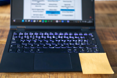 A laptop with a yellow post it on the keyboard. The post is a reminder to do somethingの写真素材