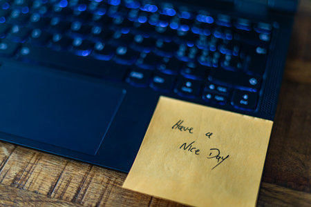 A laptop with a yellow sticky note that says Have a nice day.. The laptop is on a wooden table