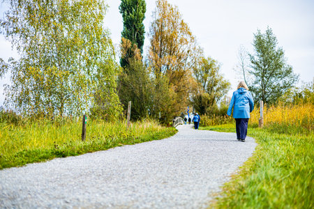A man runs in a park with trees and a lake in the background. A woman is walking behind himの写真素材