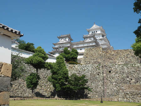Ancient samurai castle in Himeji city in Japan with white walls, dark tile roofs and stone walls on a sunny day in summer with blue sky and white cloudsのeditorial素材