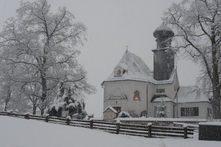 Landscape of a rural countryside with old traditional buildings on a white monochrome winter day with falling snow and snow covered trees in Europeのeditorial素材