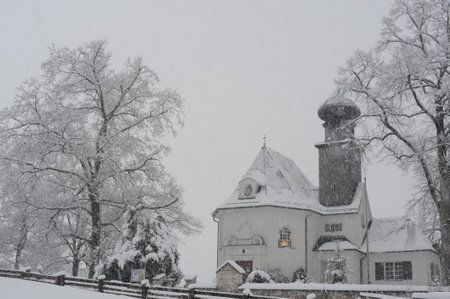 Landscape of a rural countryside with old traditional buildings on a white monochrome winter day with falling snow and snow covered trees in Europeのeditorial素材