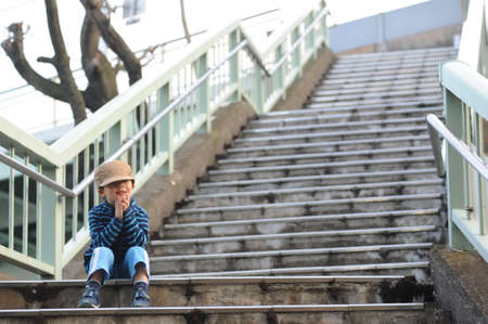 Cute and adorable young boy in blue jacket and brown cap in an industrial cityscape in a big cityの写真素材