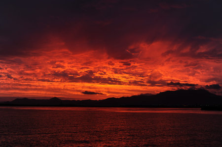 Red, pink, orange and violet sunrise at the seaside during dawn with clouds in the sky and mountains on the shore in Asiaの写真素材