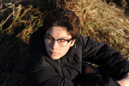 A handsome teenager boy with glasses looking into camera with serious face on a sunny day in Asia