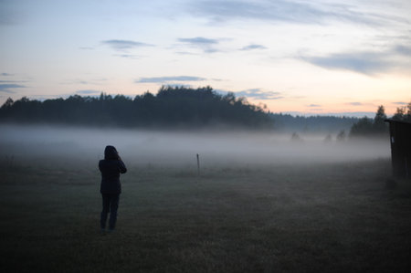 Silhouette of a woman standing in a foggy field or meadow at dawn