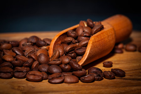 Coffee beans in wooden scoop on wooden table with dark backgroundの写真素材