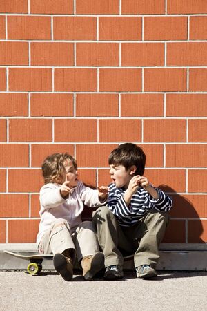 two children, brother and sister sitting against a wallの写真素材