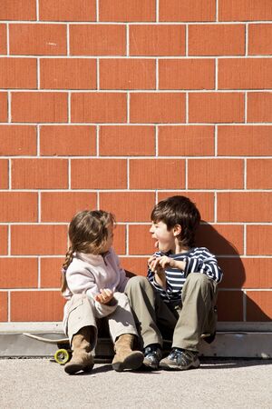 two children, brother and sister sitting against a wallの写真素材