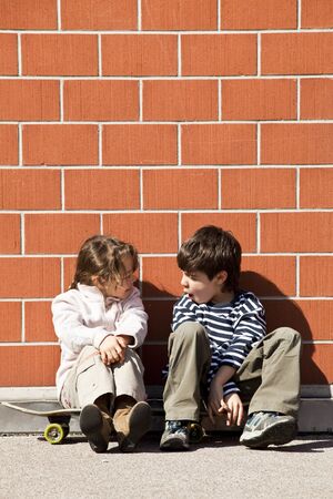 two children, brother and sister sitting against a wallの写真素材